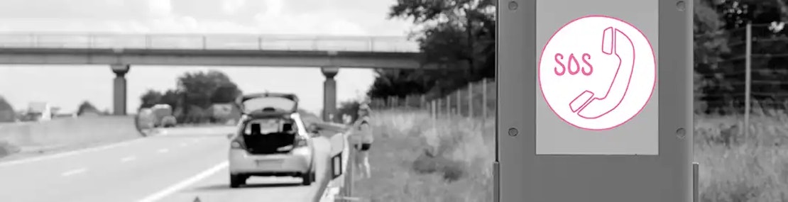 Notrufsäule an einer Autobahn – im Hintergrund ein liegengebliebenes Auto und Person in Warnweste.