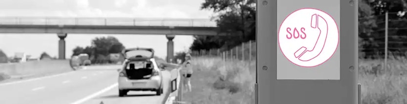 Notrufsäule an einer Autobahn – im Hintergrund ein liegengebliebenes Auto und Person in Warnweste.