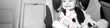 Mädchen sitzt im Auto im Kindersitz und hat Stoffteddybär in der Hand